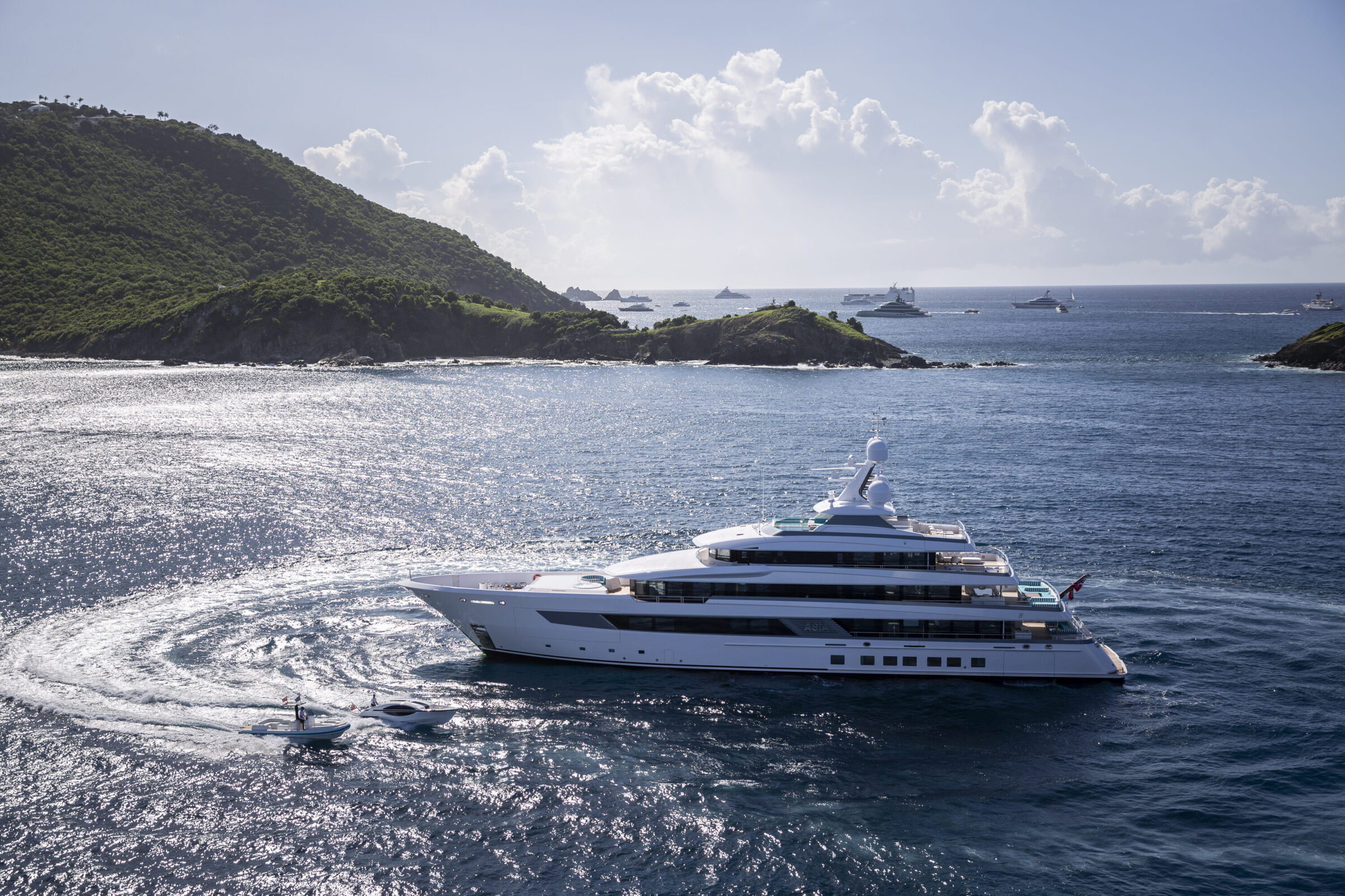 a yacht and 2 smaller boats in the water between 2 green mountains