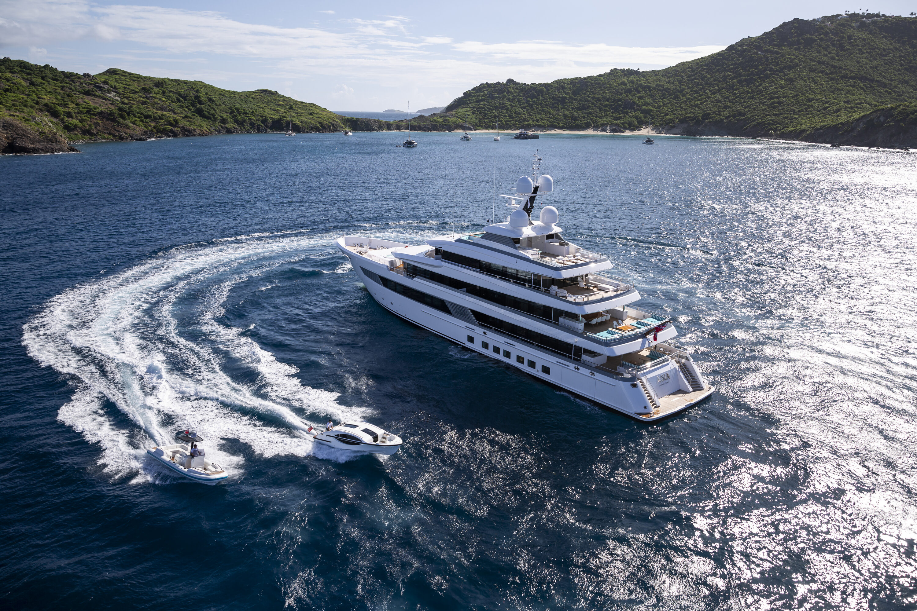 Yacht inbetween green mountains with 2 smaller boats