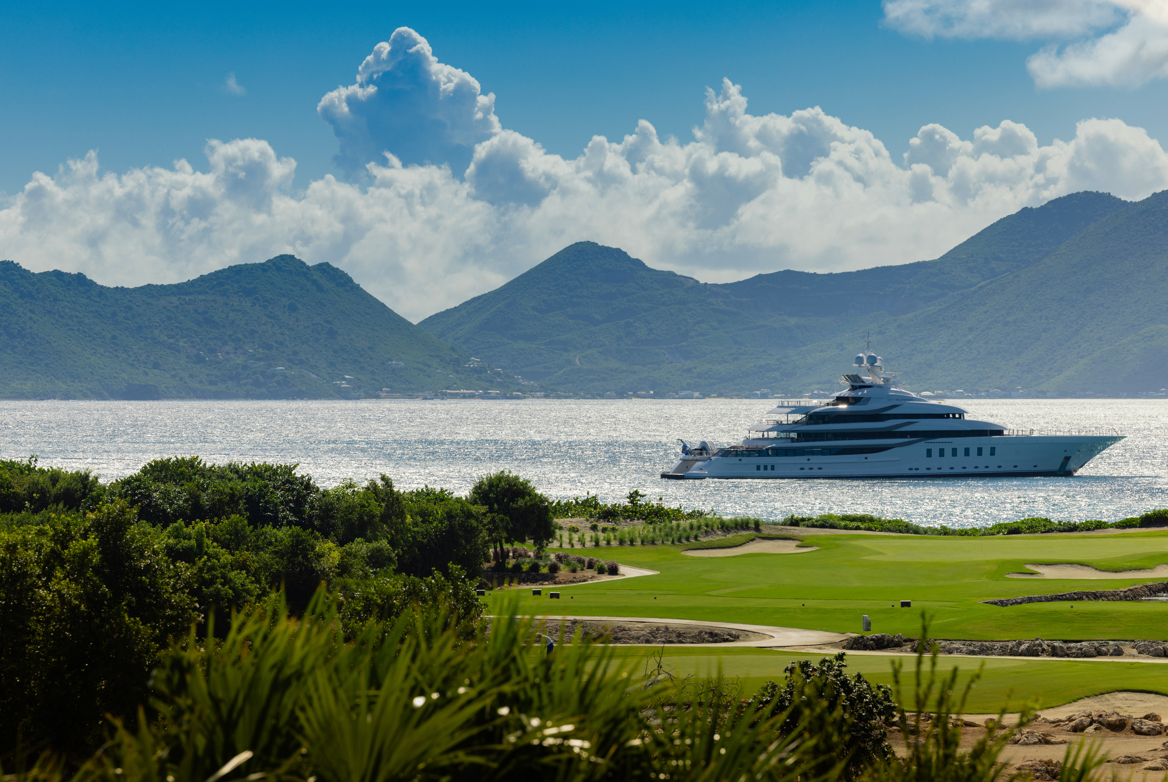 Yacht Sailing on blue waters, with green grass in the foreground and beautiful mountains in the background
